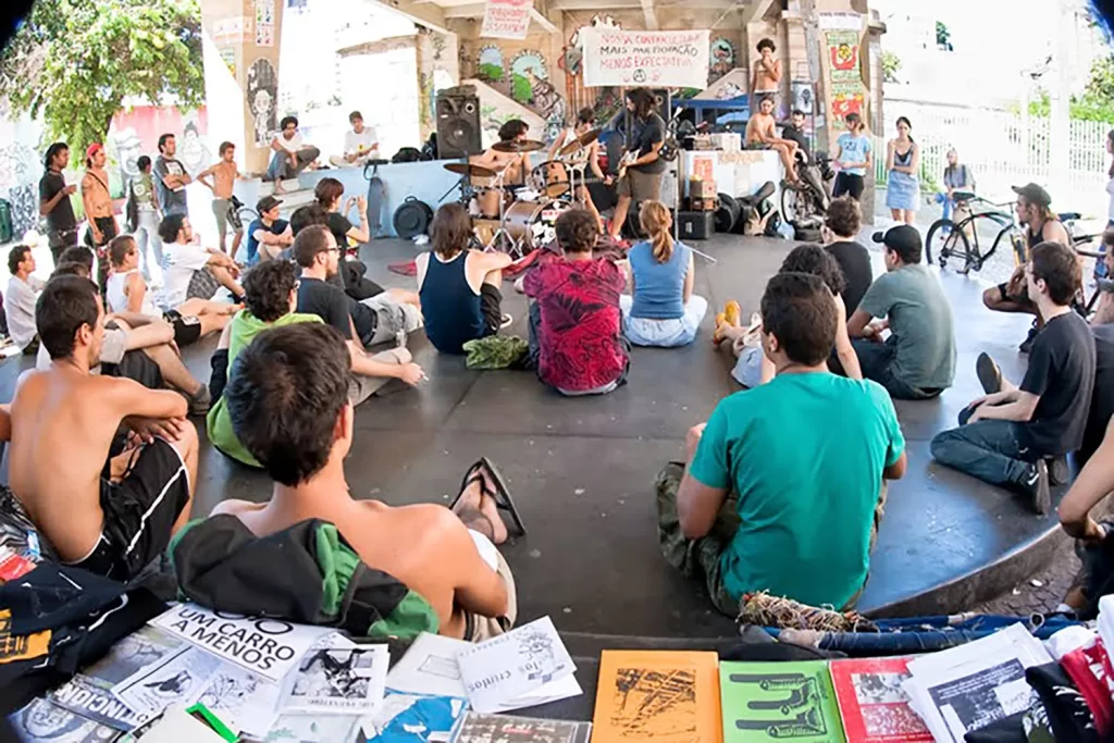 Fotografia de Ricardo Laf para a série Memórias Autorais: cena documental sob viaduto com fanzines e público jovem, unindo imagem e literatura.