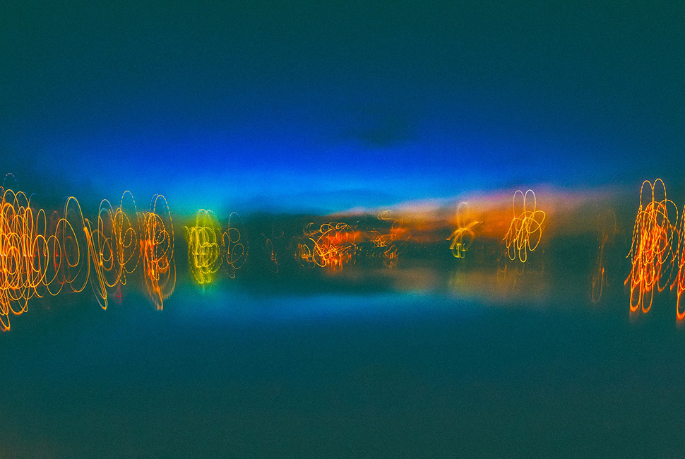 Fotografia noturna de Ricardo Laf com técnica de longa exposição, mostrando rastros de luz dourada em movimento contra um céu azul profundo no Circuito Pampulha.