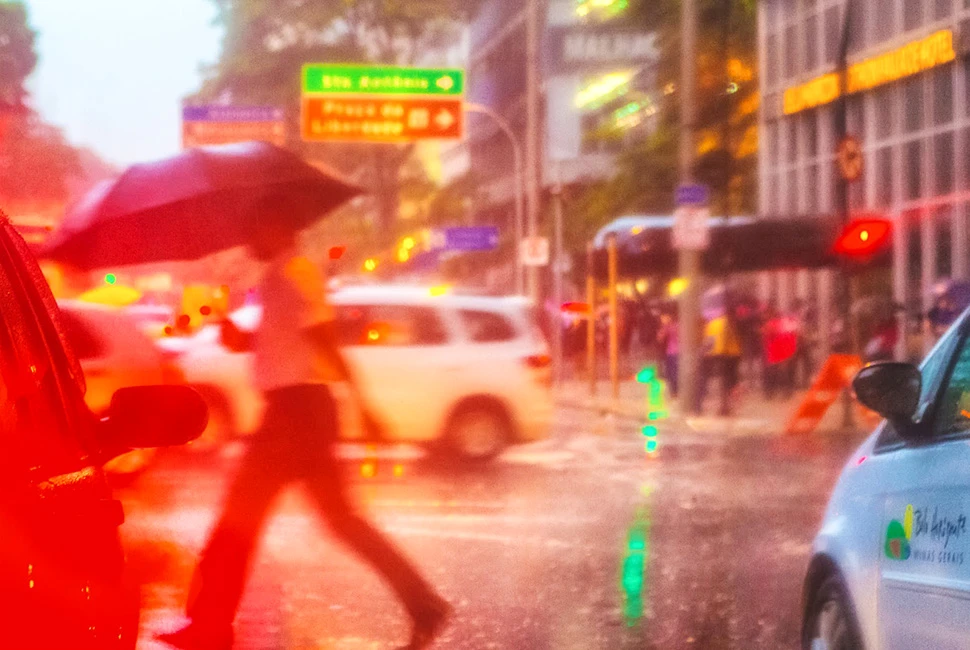 Fotografia urbana com efeito de longa exposição ou desfoque de movimento, mostrando o tráfego e luzes coloridas do centro de Belo Horizonte sob chuva, com tons vibrantes de laranja, vermelho e azul.