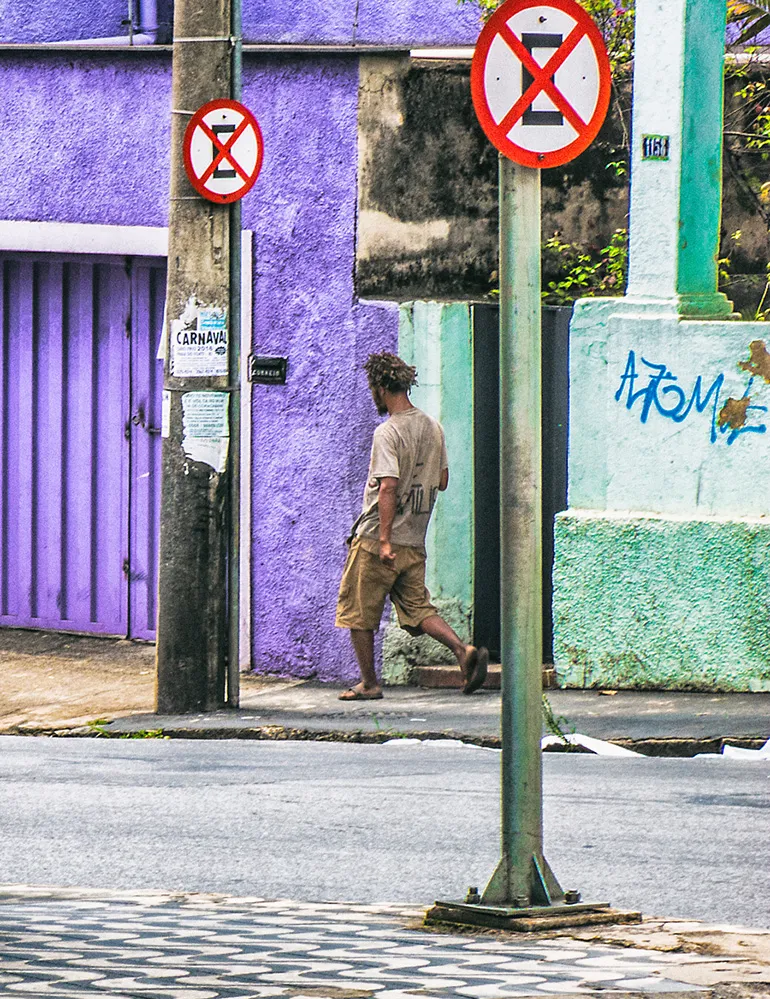 Fotografia autoral de uma cena urbana na região noroeste de Belo Horizonte, retratando uma rua com sinalização de trânsito e uma figura solitária ao fundo, sugerindo o tema do deslocamento e da exclusão.