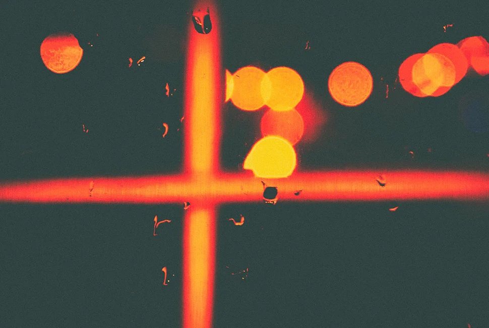 Fotografia abstrata de Ricardo Laf mostrando pontos de luz circulares e alaranjados (bokeh) através de uma janela com gotas, criando um efeito de luz incandescente e fragmentada.