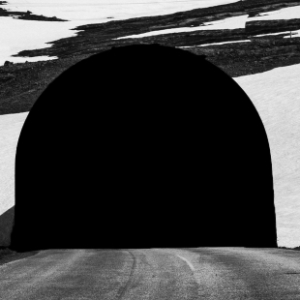 Fotografia autoral de Ricardo Laf mostrando a entrada em arco de um túnel de pedra na Islândia, com a luz do dia visível ao fundo.