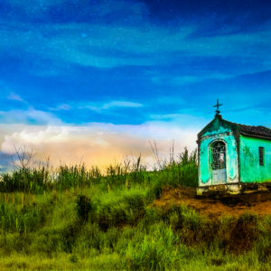 Fotografia autoral de Ricardo Laf de uma pequena capela verde à beira da estrada em Conceição dos Ouros, Minas Gerais, sob um céu azul intenso com nuvens esparsas.