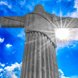 Fotografia autoral de Ricardo Laf da Estátua de Cristo Rei no Barreiro, Belo Horizonte, com o sol criando um efeito de luz radiante por trás da escultura contra um céu azul.