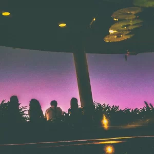 Fotografia autoral de Ricardo Laf capturando o reflexo da Casa do Baile e de silhuetas humanas nas águas do lago de seus jardins, com tons de crepúsculo.