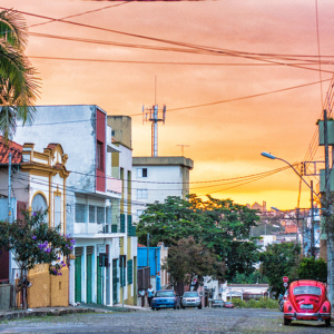 Fotografia autoral de Ricardo Laf mostrando um Fusca vermelho estacionado em uma rua da Região Leste de Belo Horizonte, com arquitetura urbana e céu ao entardecer.