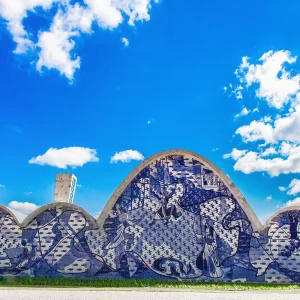 Fotografia de Ricardo Laf da Igreja de São Francisco de Assis na Pampulha, Belo Horizonte, destacando as curvas de Oscar Niemeyer e o painel de azulejos de Portinari sob um céu azul.