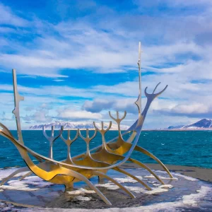 Fotografia de Ricardo Laf da escultura Sólfar em Reykjavik, Islândia, destacando a estrutura metálica em formato de barco contra o mar e montanhas ao fundo.