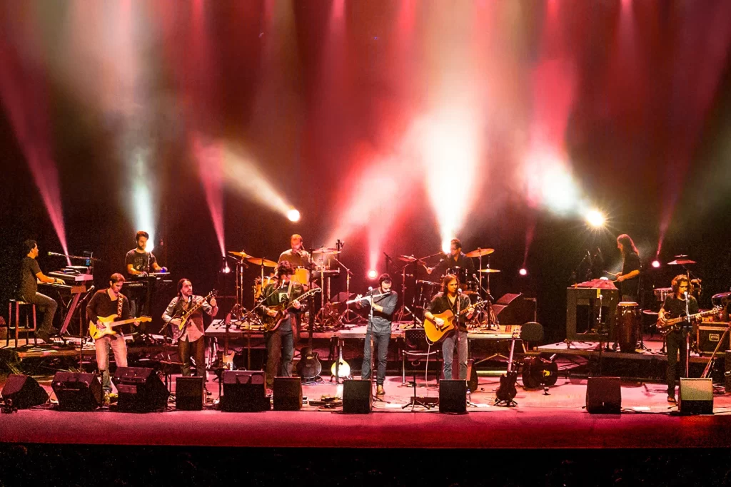 Plano aberto dos integrantes da Orquestra Mineira de Rock sob potentes fachos de luz branca no Sesc Palladium.