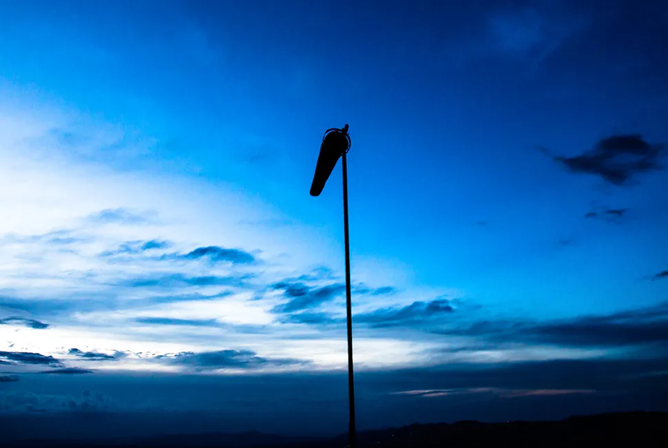 Fotografia de Ricardo Laf mostrando uma biruta preta esticada pelo vento contra um céu de crepúsculo azul escuro na Serra da Moeda, Minas Gerais.