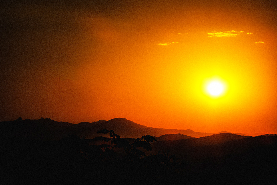 Fotografia de Ricardo Laf capturando o sol poente como um disco dourado intenso sobre a silhueta das montanhas da Serra da Moeda, em Minas Gerais.