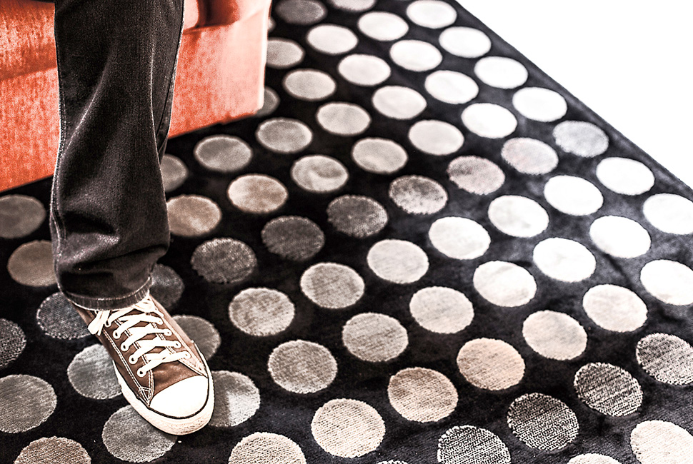 Foto de Ricardo Laf mostrando em close um tênis marrom sobre um tapete preto com padrão de bolinhas brancas em relevo.