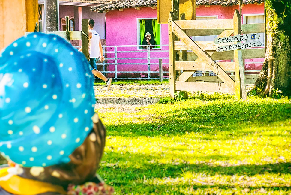 Foto de Ricardo Laf mostrando em primeiro plano o detalhe da escultura "Sinhá" com padrão de bolinhas azuis, e ao fundo, um homem caminhando pela rua e uma mulher na janela em Lavras Novas.