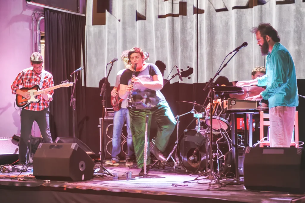 Fotografia de Ricardo Laf apresentando Juliana Perdigão e músicos em cena, destacando a interação no palco sob iluminação suave que valoriza a profundidade e a harmonia do conjunto.