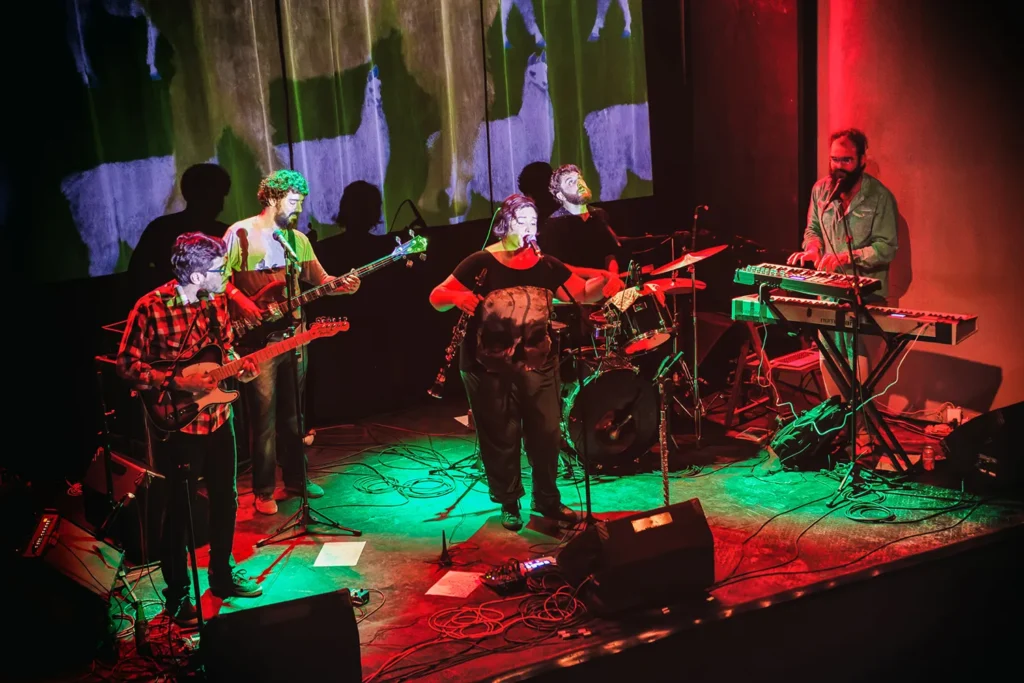 Fotografia de Ricardo Laf registrando a dinâmica de palco de Juliana Perdigão e sua banda, com iluminação cênica que enfatiza a composição e a profundidade da cena musical.