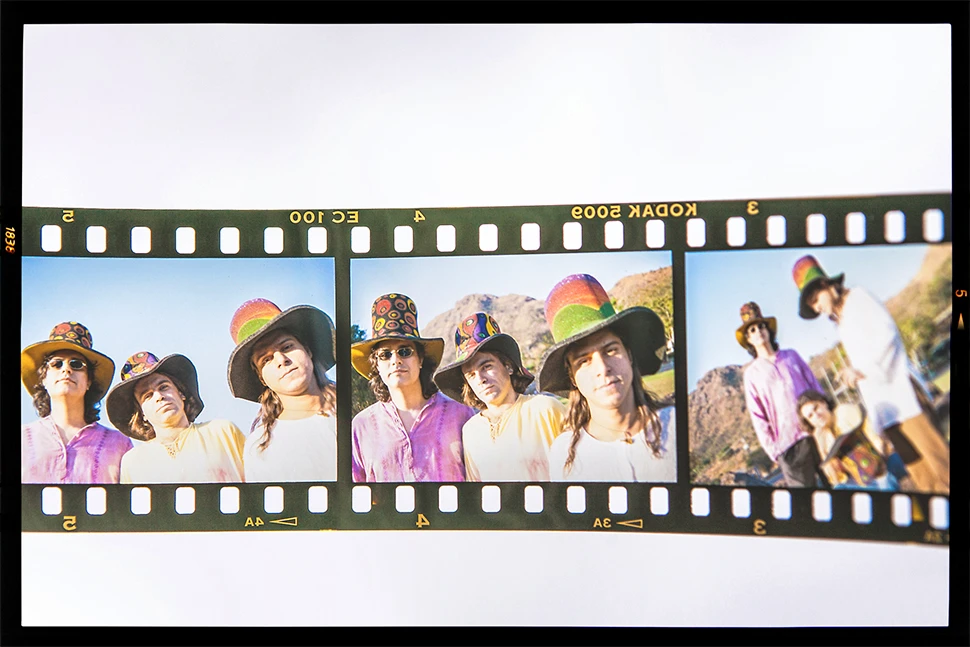 Fotografia autoral de Ricardo Laf apresentando três fotogramas sequenciais de um filme positivo (Cromo) dos anos 90; a imagem mostra o trio original da banda Somba usando chapéus coloridos em um cenário externo, com a borda do negativo Kodak visível.