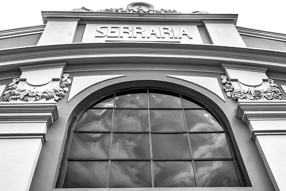 Fotografia em preto e branco com foco em close na fachada da Serraria Souza Pinto em Belo Horizonte, destacando as janelas em arco e a textura da arquitetura histórica em estilo eclético.