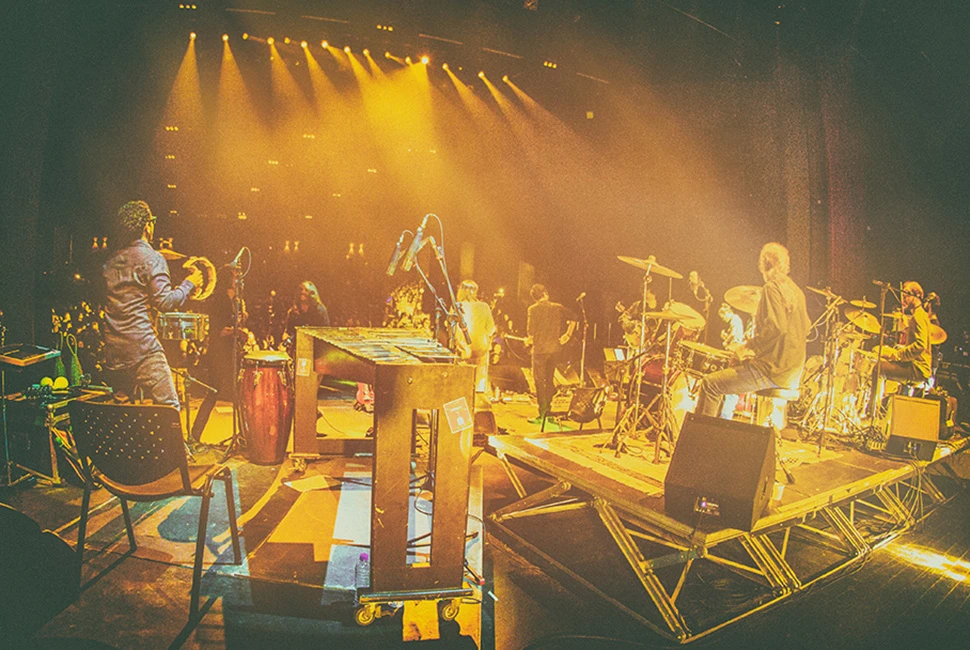 Fotografia da Orquestra Mineira de Rock no Sesc Palladium. Feixes de luz amarelos cruzando o palco com músicos em atuação e efeito de neblina cenográfica.