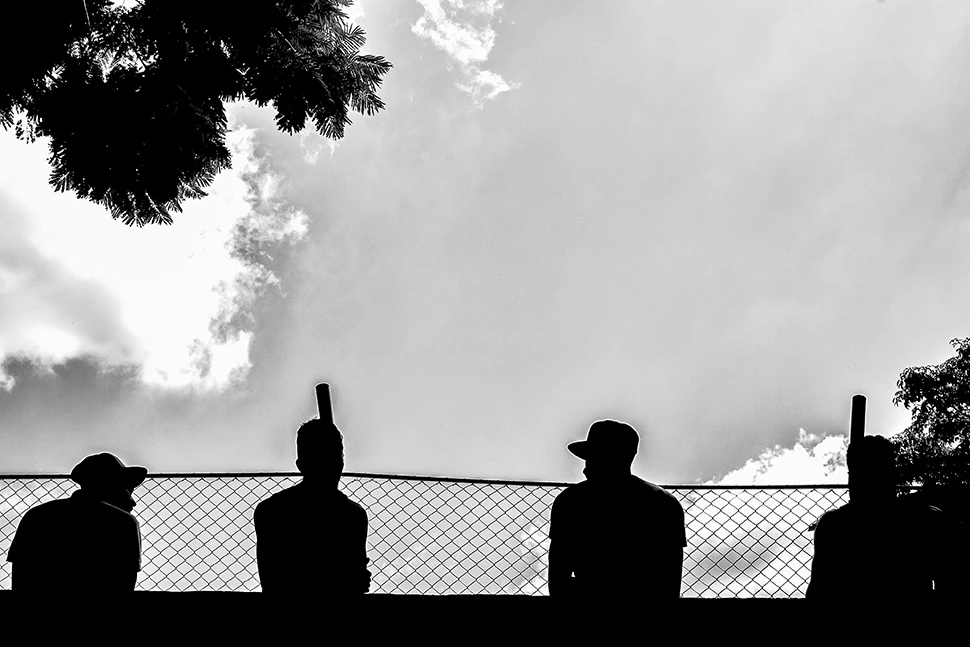 Silhuetas de três homens (fogueteiros) aguardando o início de uma partida de futebol amador na região nordeste de Belo Horizonte, por Ricardo Laf.