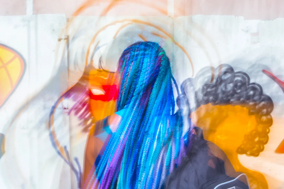 Jovem de costas com dreads azuis e coloridos contemplando um mural de arte urbana vibrante no hipercentro de Belo Horizonte, fotografia de Ricardo Laf.