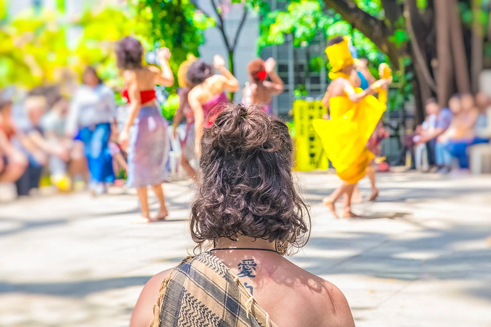 Performance artística na área externa do Museu Histórico Abílio Barreto, com artista em destaque e público ao fundo sob luz natural, fotografia de Ricardo Laf.
