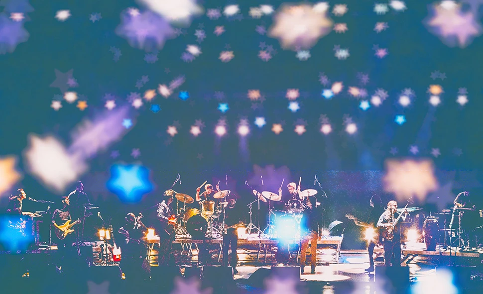 Fotografia de palco da Orquestra Mineira de Rock no Teatro Bradesco. Músicos em performance sob iluminação azul e pontos de luz difusos.