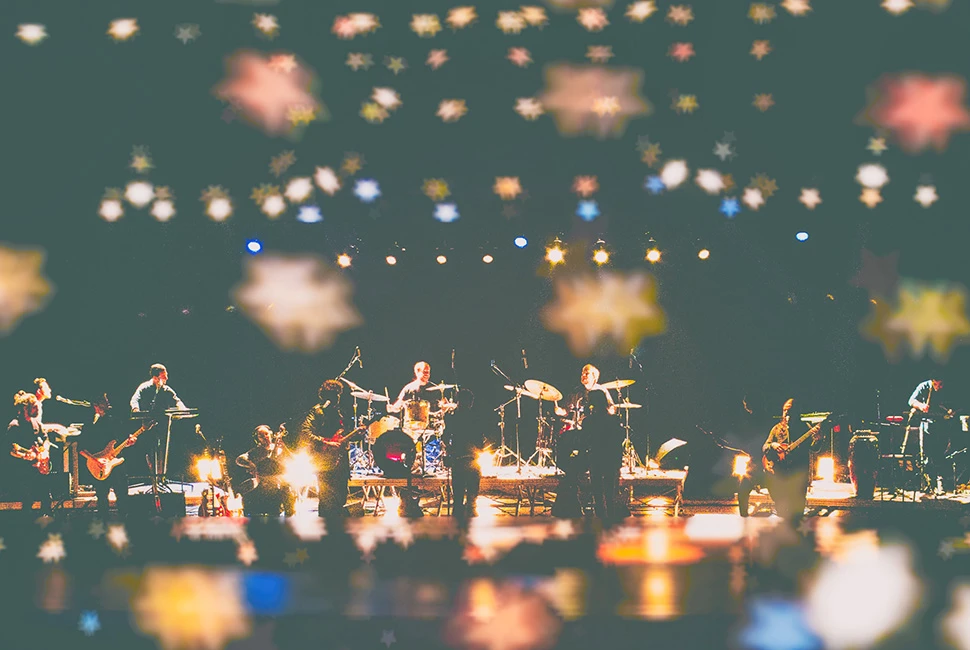 Vista panorâmica da Orquestra Mineira de Rock no Teatro Bradesco. Músicos no palco sob feixes de luz dourada e atmosfera de grande espetáculo.