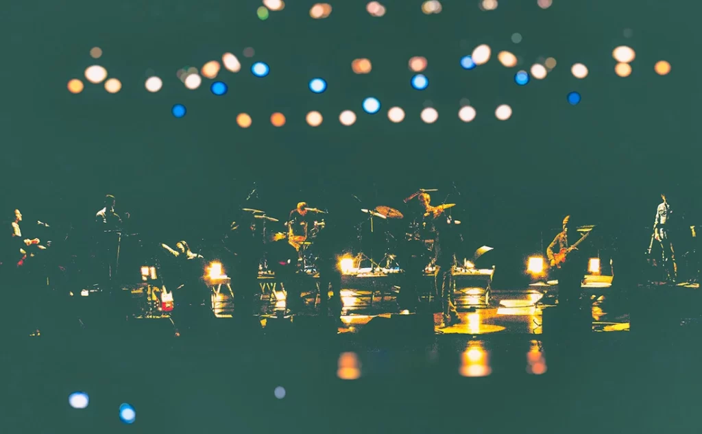 Fotografia de palco da Orquestra Mineira de Rock com músicos em silhueta contra luzes de fundo circulares (bokeh). Registro em teatro.
