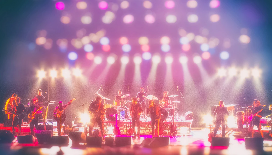 Fotografia de palco da Orquestra Mineira de Rock com iluminação branca brilhante e efeito de flare. Músicos em performance dinâmica no Teatro Bradesco.