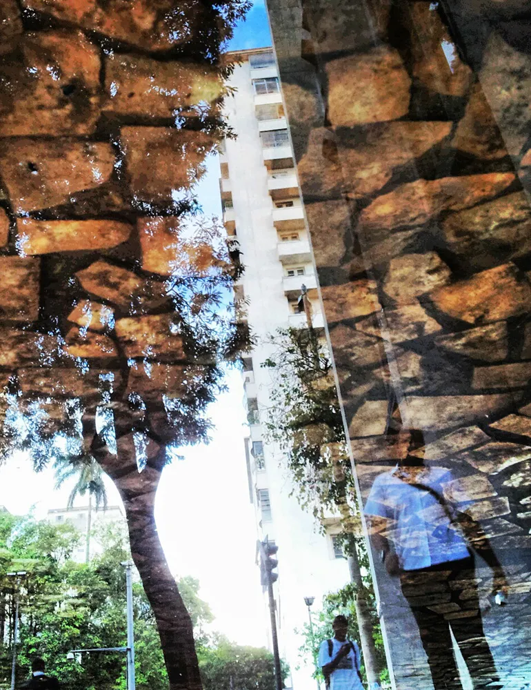 Composição vertical capturando o reflexo de prédios e árvores do centro de Belo Horizonte em uma superfície de vidro, com tons ocres, terrosos e azulados que criam uma abstração urbana.