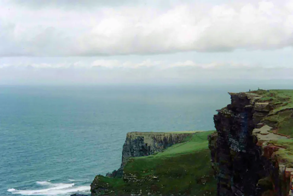 Fotografia de Ricardo Laf capturando as monumentais falésias dos Cliffs of Moher na Irlanda, com o oceano batendo contra as rochas sob céu nublado.