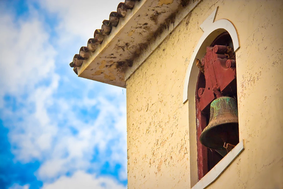 Fotografia autoral de Ricardo Laf capturada em ângulo contra-plongée, destacando um sino de bronze antigo em uma torre de igreja colonial em São Gonçalo do Rio Abaixo, Minas Gerais.