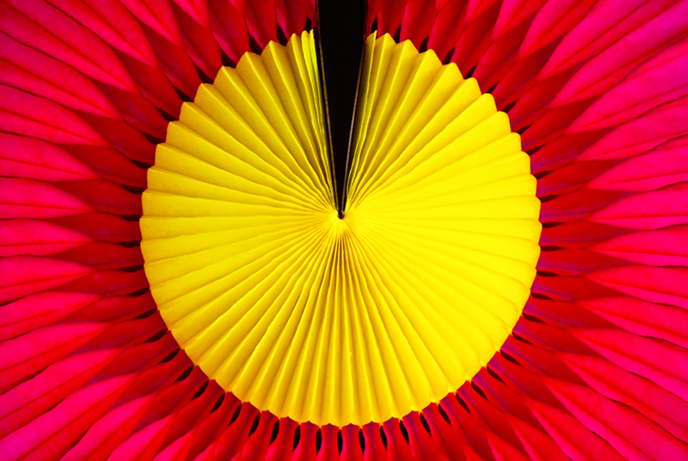 Foto de Ricardo Laf mostrando o detalhe em close de um adereço em espiral com centro amarelo e camadas externas em tons de rosa e vermelho vibrante.