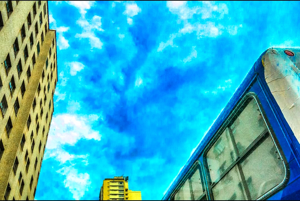 Fotografia de Ricardo Laf feita de dentro de um veículo no trânsito de Belo Horizonte. A imagem mostra uma composição de fragmentos arquitetônicos e a lateral de um ônibus, destacando a dinâmica urbana do centro.