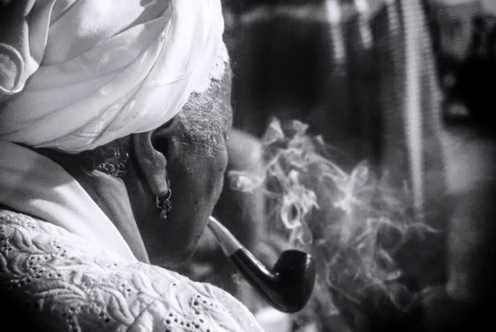 Fotografia em preto e branco de Ricardo Laf durante a Festa do Preto Velho na Praça 13 de Maio, em Belo Horizonte. A imagem mostra o detalhe da fumaça de um cachimbo, simbolizando o ritual e a devoção das comunidades de matriz afro-brasileira.