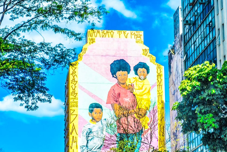 Foto de Ricardo Laf registrando um grande painel de arte urbana (grafite) na lateral de um edifício no centro de Belo Horizonte. A imagem destaca as cores vibrantes da pintura contra a arquitetura urbana e o céu ao fundo.