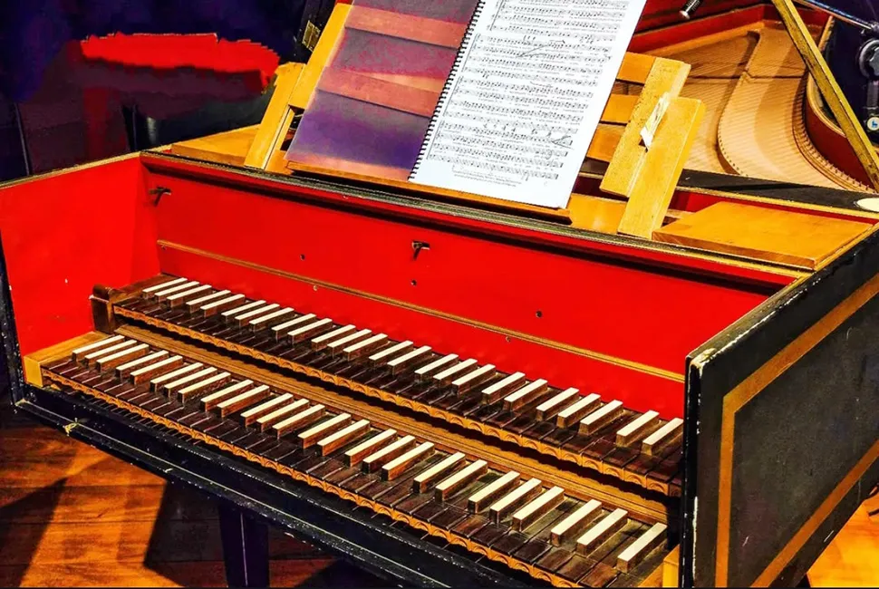 Foto de Ricardo Laf capturando em close os detalhes de um cravo, destacando as teclas, as cordas metálicas e a estrutura decorada em vermelho e dourado.
