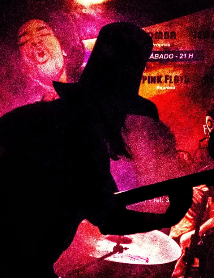 Fotografia de Ricardo Laf registrando performance da Banda Somba em Belo Horizonte, com iluminação vermelha intensa e cartaz do Pink Floyd ao fundo.