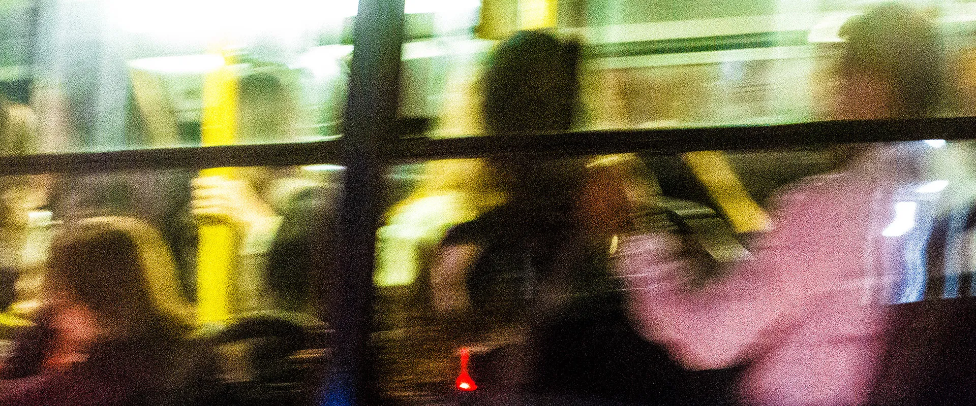 Fotografia urbana de Ricardo Laf registrando o interior de um ônibus à noite através do vidro, com reflexos em tons amarelos, verdes e pretos e vultos em movimento.