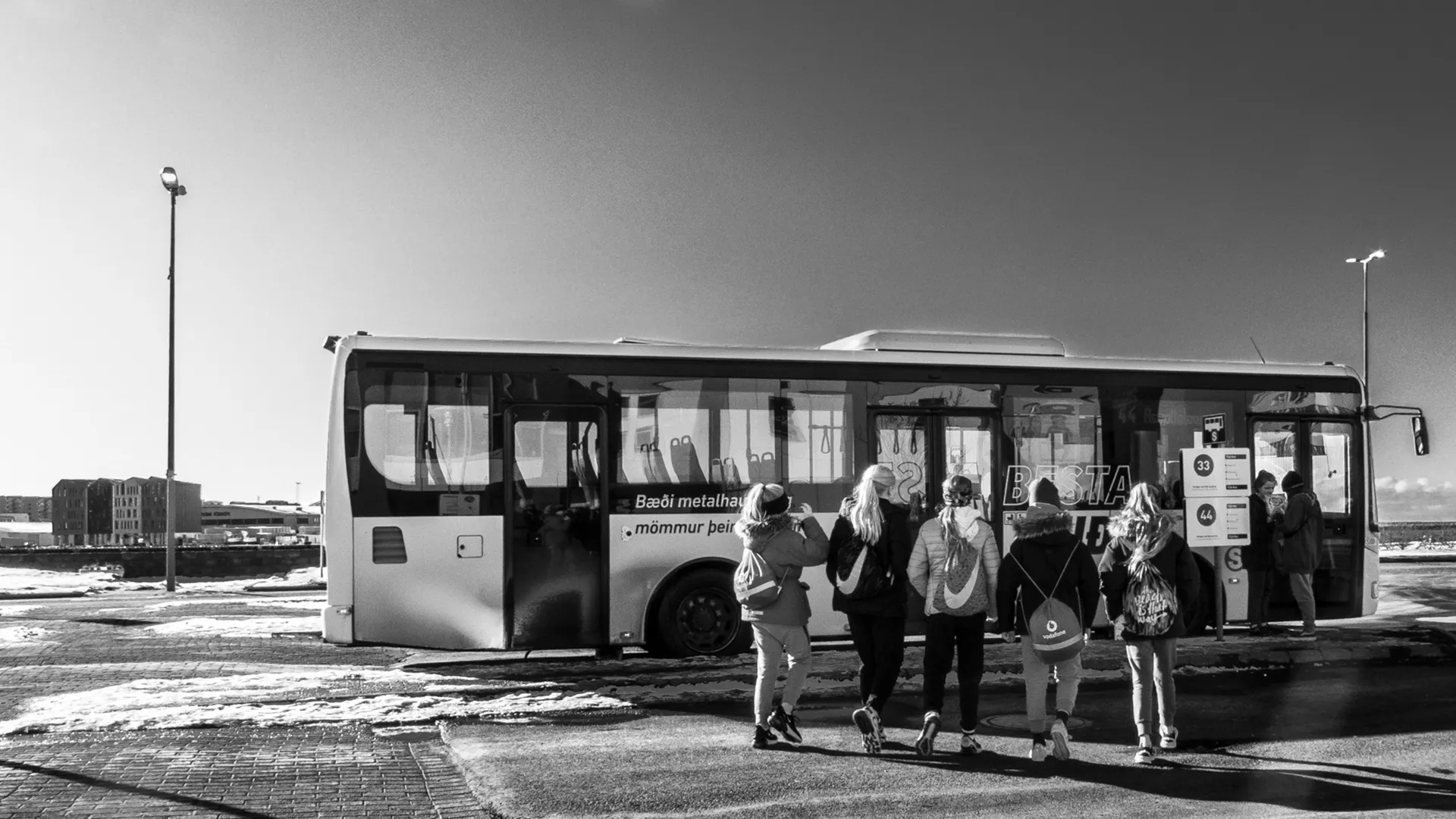 Fotografia urbana em preto e branco de um ônibus de transporte público estacionado em Reykjavik, Islândia. Em primeiro plano, pessoas de costas caminham em direção ao veículo sob um céu com nuvens dispersas. Foto: Ricardo Laf.