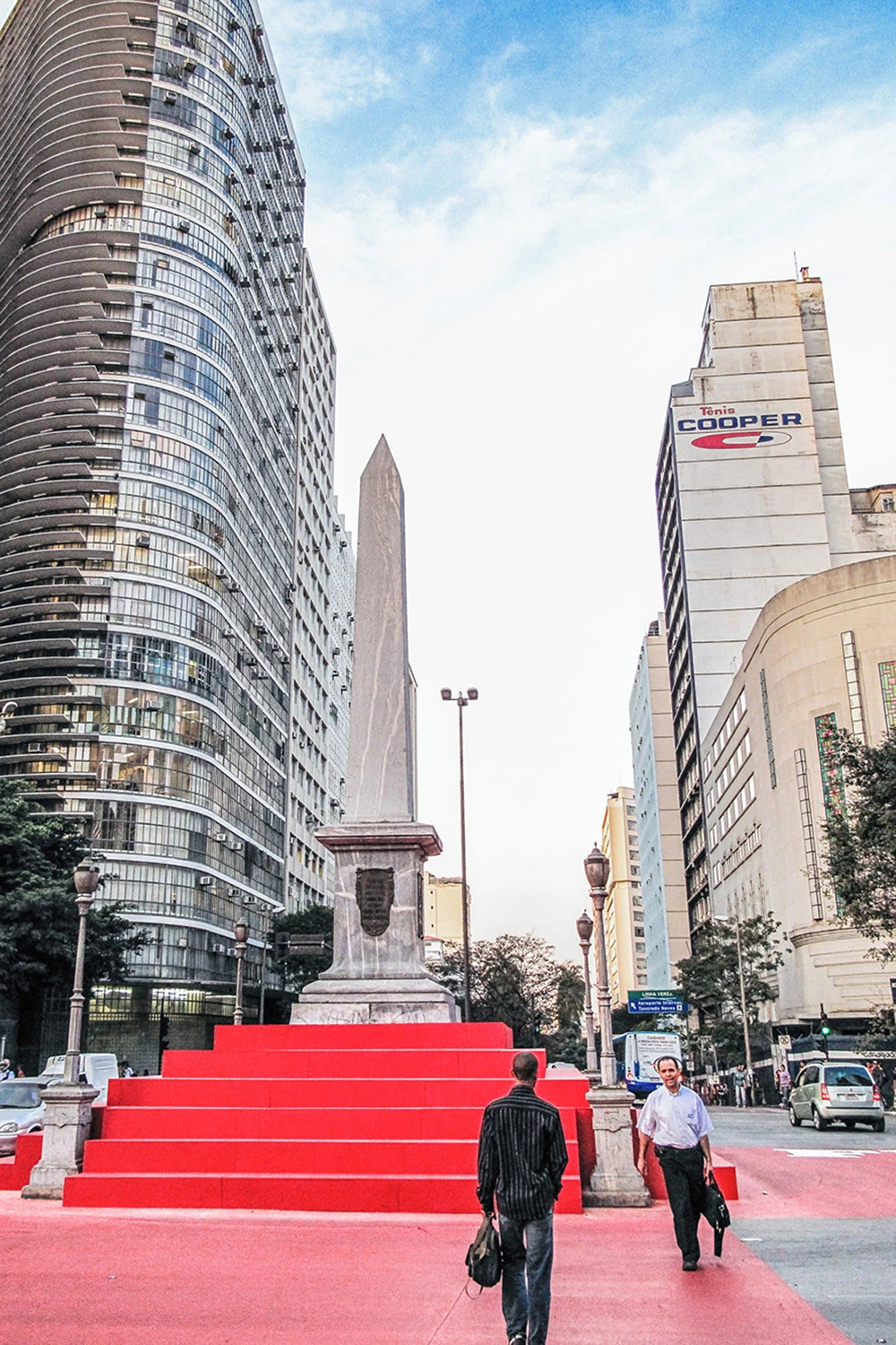 Obelisco de pedra conhecido como Pirulito erguido no centro da Praça Sete de Setembro, cercado por edifícios e transeuntes em Belo Horizonte.
