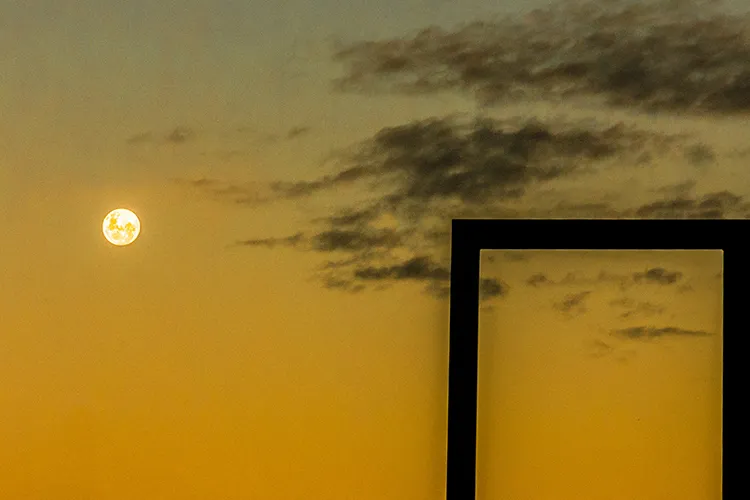 Fotografia autoral de Ricardo Laf mostrando o sol ou a lua em um céu amarelado, emoldurado por uma estrutura geométrica escura em primeiro plano.