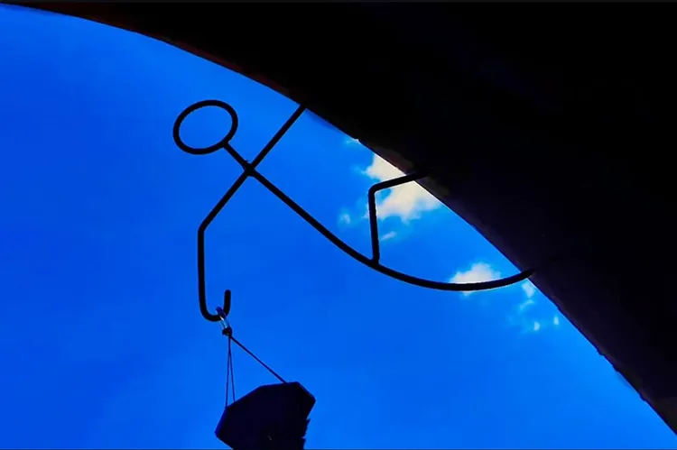 Escultura em ferro de figura humana contra o céu azul intenso fotografada com smartphone