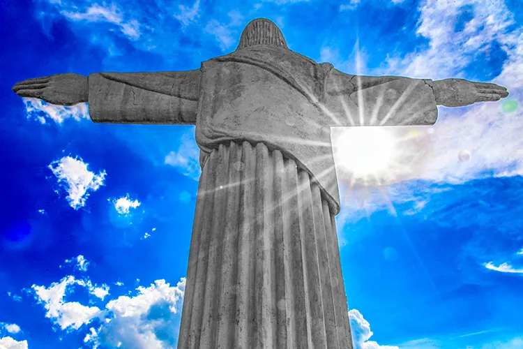 Vista contra o céu da estátua do Cristo Rei na região do Barreiro em Belo Horizonte, com os braços abertos sobre a paisagem urbana.