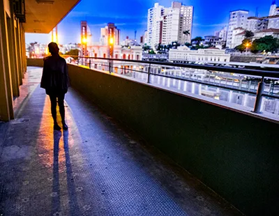 Fotografia ao crepúsculo no Baixo Centro de Belo Horizonte, mostrando uma figura em performance sob iluminação urbana aquecida, com prédios e o céu ao fundo.