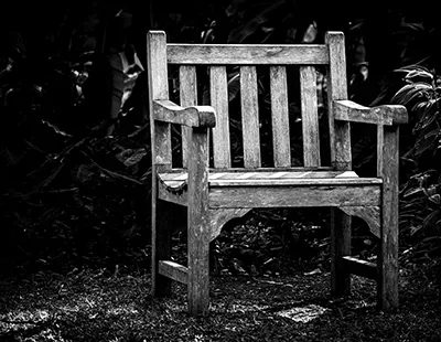 Fotografia em preto e branco de uma cadeira rústica de madeira em ambiente de iluminação lateral e sombras marcadas.