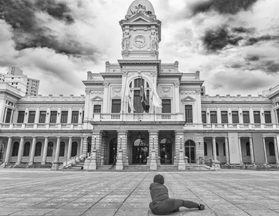 Fotografia em preto e branco do prédio histórico da Praça da Estação em Belo Horizonte, com uma figura no primeiro plano contemplando a arquitetura.
