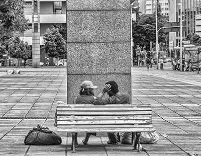 Fotografia em preto e branco de um casal sentado em um banco de madeira na Praça da Estação em Belo Horizonte.