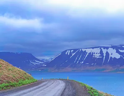 Fotografia de paisagem contemplativa da costa de Hvammstangi na Islândia com montanhas cobertas de neve ao fundo e águas calmas.