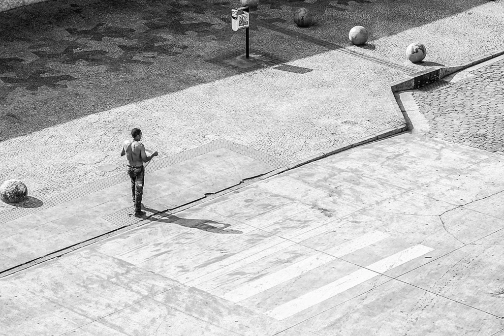 Fotografia em preto e branco com perspectiva geométrica do centro de Belo Horizonte, mostrando um homem caminhando solitário em uma praça com esferas de concreto.